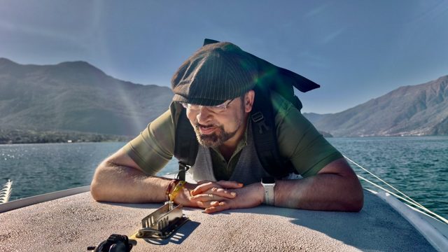 Sören auf einem Boot, im Hintergrund ein See und Berge